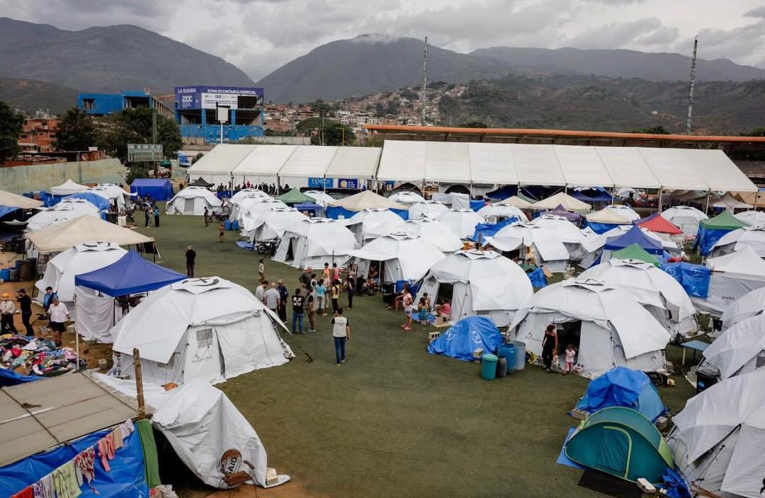 An aerial view of an emergency shelter camp with rows of relief tents beneath mountains