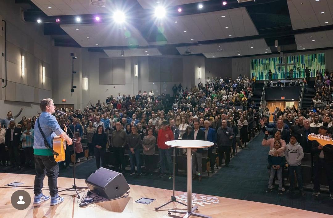 A worship leader on stage in front of a standing congregation